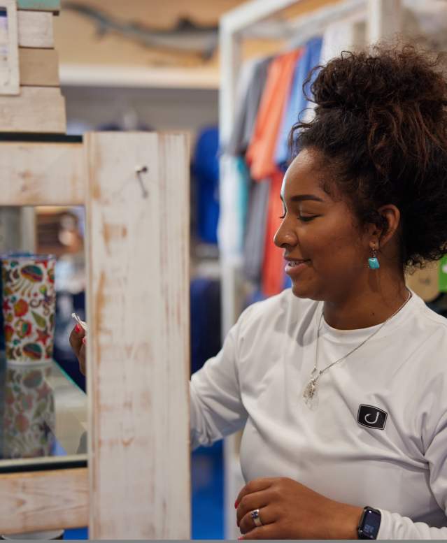 woman in long sleeve white shirt reaching for multi-color cups on shelf.