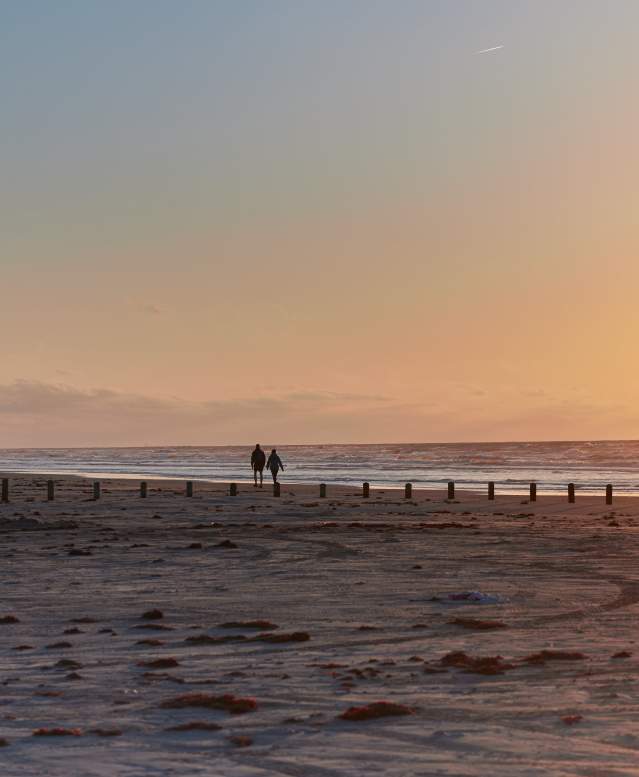 A silhouetted couple walks along the beach at sunrise. A golf cart is parked in the distance.