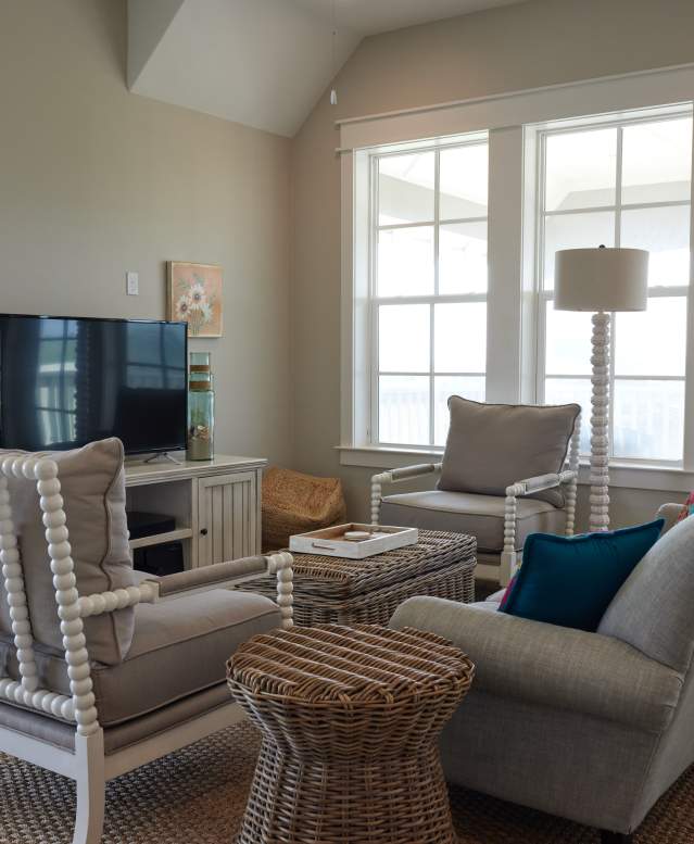 A living room with coastal decor in shades of beige. A tan couch faces a television and two chairs face each other perpendicular to the couch.