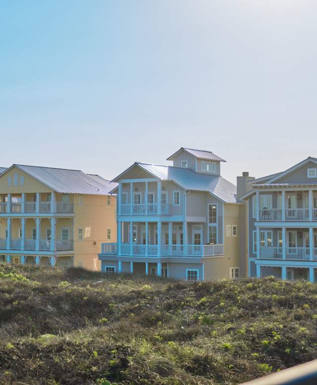 row of 4 large beach houses nestled in dunes in bright sunlight