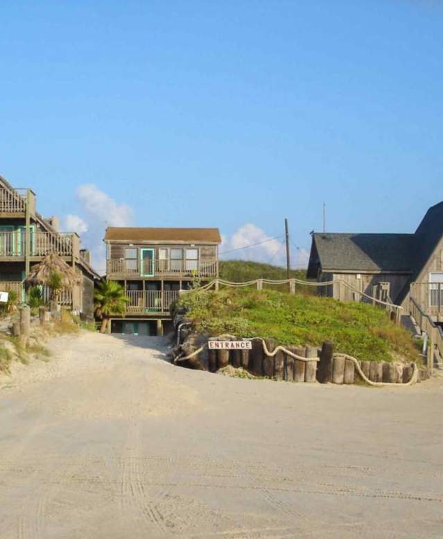 View of Sandollar Sity lodging taken from the beach. Three visible buildings, two triangular-shaped roofs on either end and a flat roofed building in the middle.