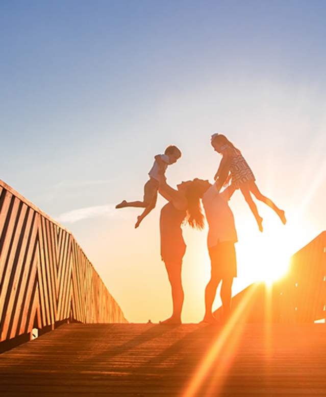 Parents lift their two children in the air on a boardwalk at sunrise in Port Aransas. Texas