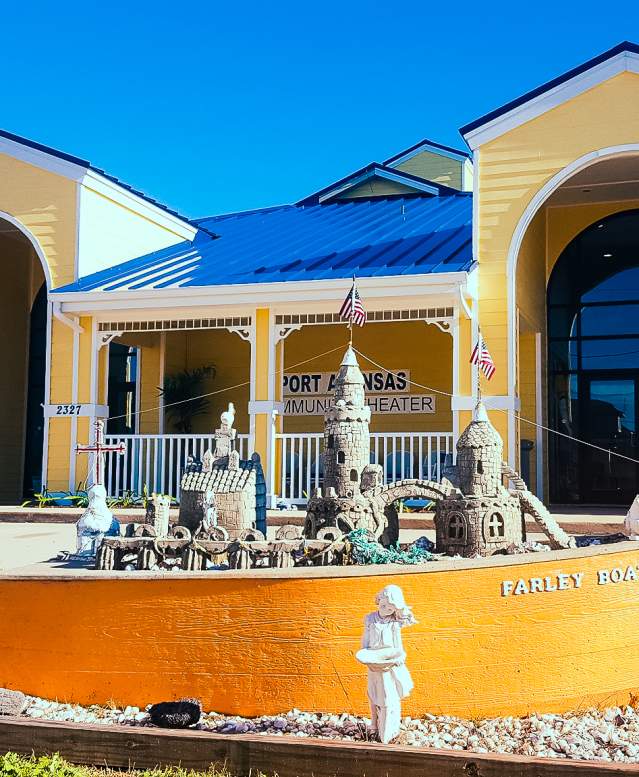 Yellow Farley boat with a small sandcastle inside sits in front of a large yellow building with a blue metal roof