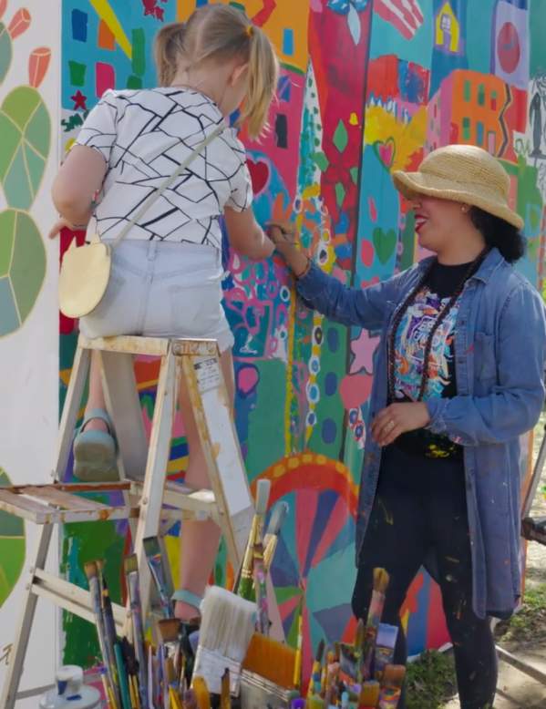 A painter helping two children paint a mural