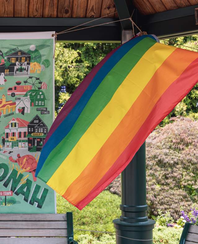 A Pride flag is gently blowing in the wind in front of a sign that reads "Katonah."