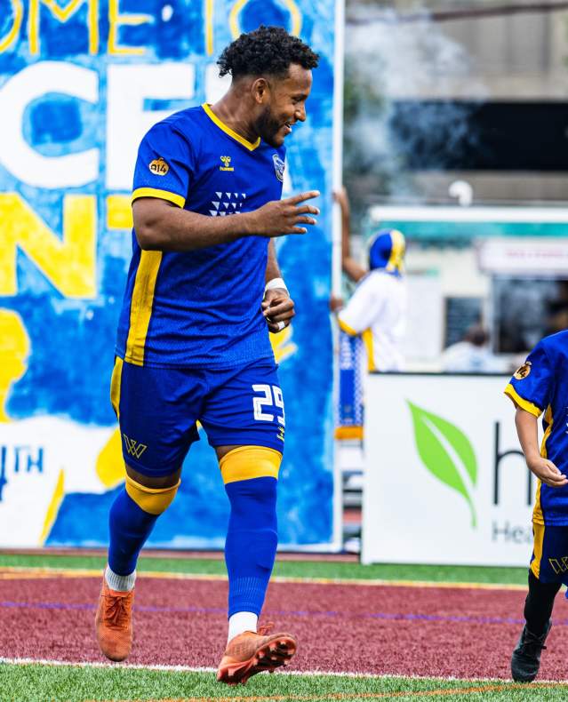 A Westchester Soccer Club player runs out onto the field accompanied by a youth player.