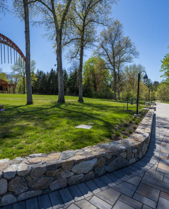 The entry path to Caramoor, surrounded by trees and with a piece of red artwork in the shape of the letter "c".