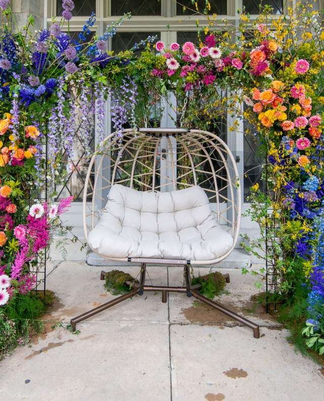 An arch of multi-colored flowers surrounds a bench with seating for two.