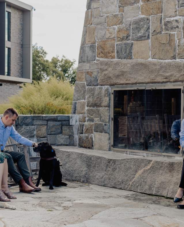 Four people and two guide dogs sit together chatting at a firepit.