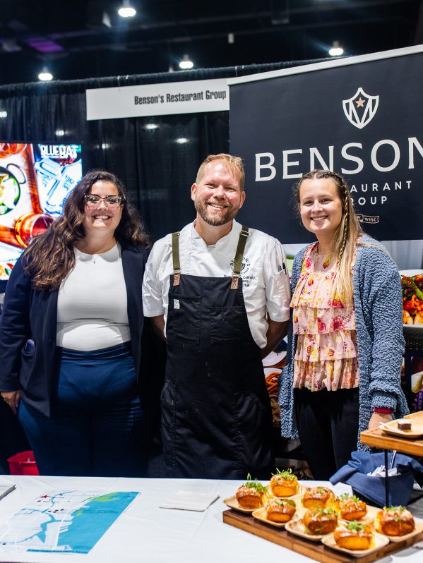woman, man, and another woman smiling at a booth displaying lobster rolls and smores pie