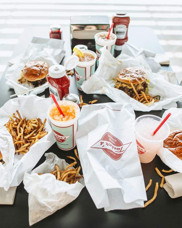 A table filled with fries, cheeseburgers and soft drinks at Tucker's Onion Burgers
