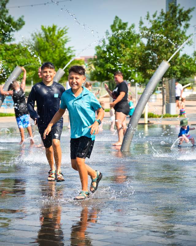 Kids running around the splash pad at Scissortail Park