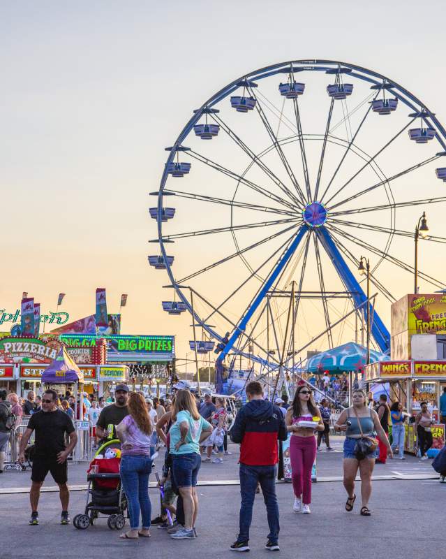 People walking around the Oklahoma State Fair with a view of the Ferris wheel in the background
