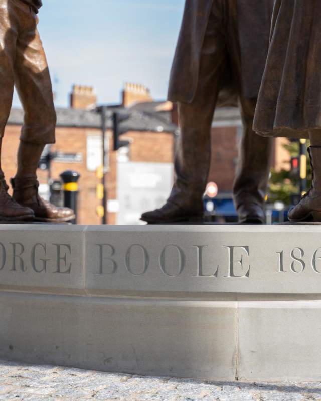 A statue of George Boole outside Lincoln Train Station in the sunlight