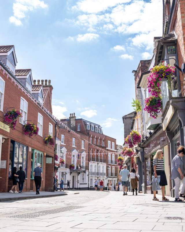 Lincoln's Bailgate street view with shopfronts and bunting on a sunny day with people shopping and walking along the pavement.