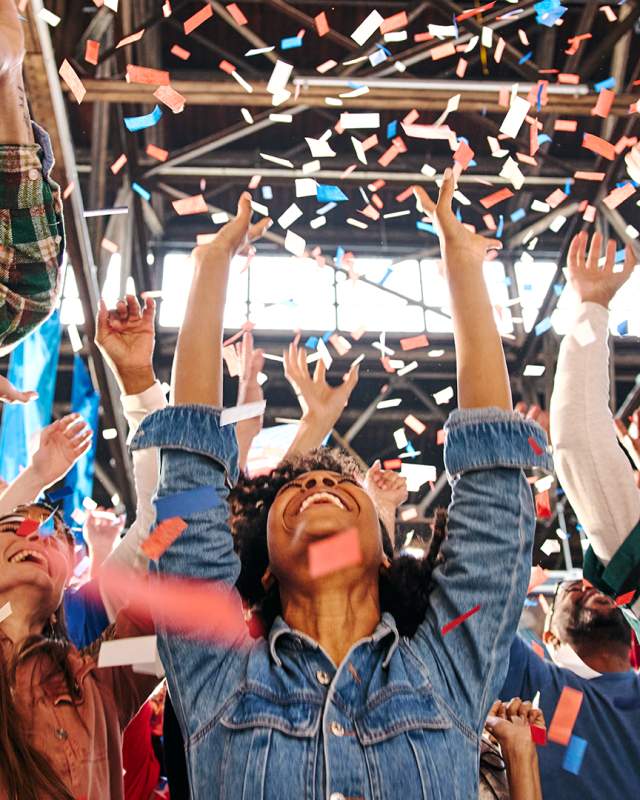 People with their arms up, cheering and confetti falls on them