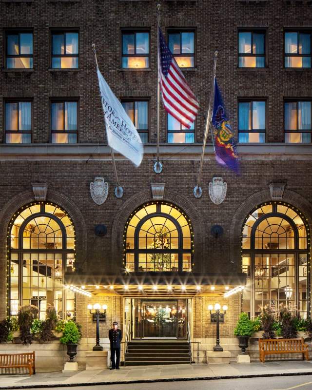 An exterior of a historic hotel with three flags hanging off the entrance at night