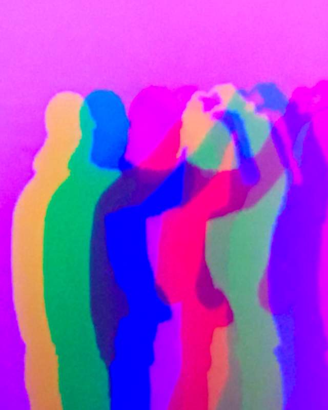 Two people posing in front of a pink screen casting colourful shadows on the wall