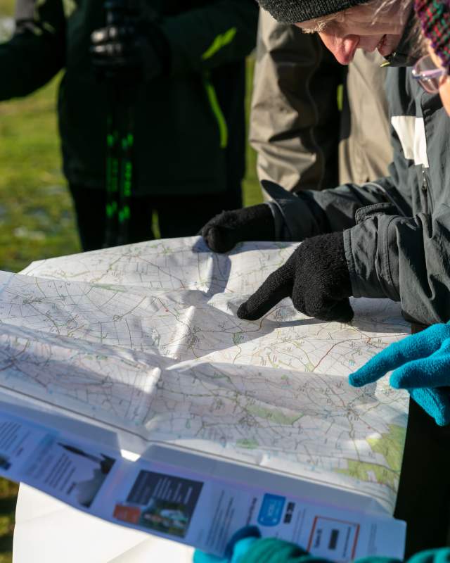 A group of people dressed in winter clothes holding a map and pointing at locations.
