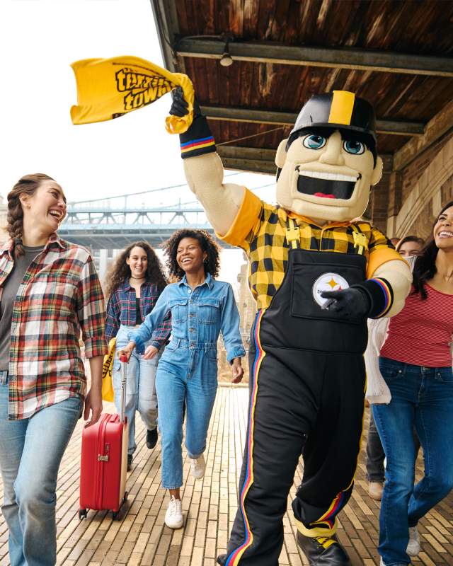 A group of people walking with a large mascot who is waving a yellow towel in the air