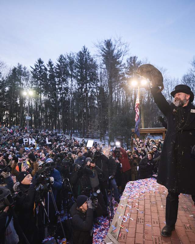Man in a top hat lifting up a groundhog in front of a large crowd for Groundhog Day in Punxsutawney