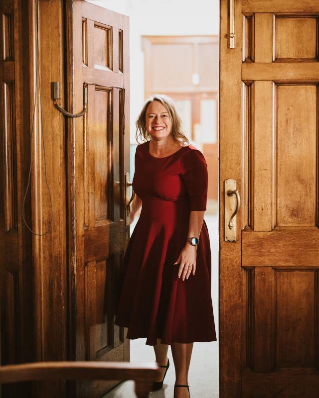 a woman in a red dress entering through large old wooden doors