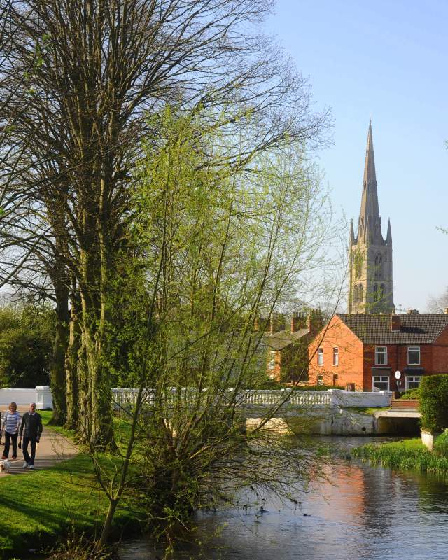 Man and woman walk their dog along the river side with church in background