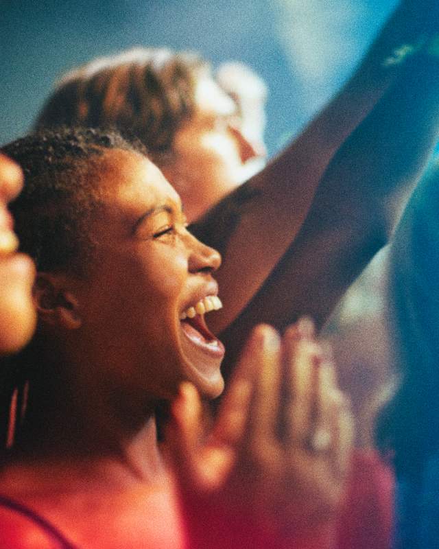 A woman in a crowd cheers with fellow fans.