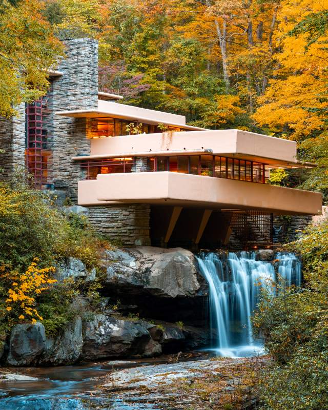 Iconic architectural building Fallingwater sits atop a waterfall with fall foliage surrounding.