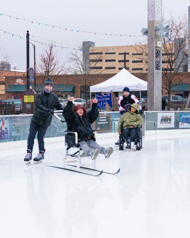 Two men being pushed on wheelchair accessible Ice skates at Main Street square in Rapid City South Dakota