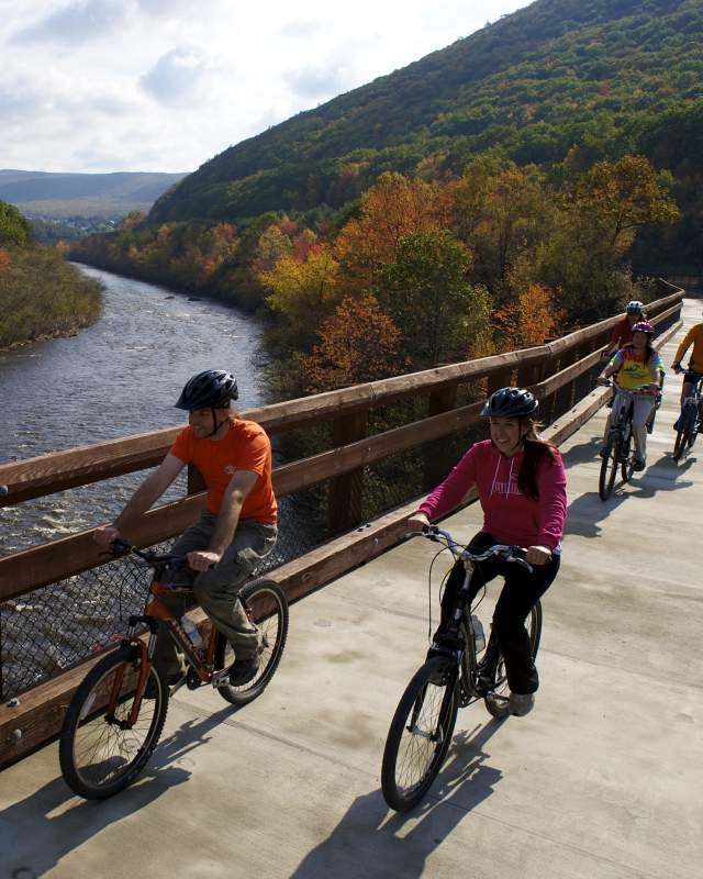 Family bikes across a bridge with mountains and river in the background