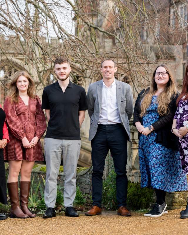 The Meet Cambridge team: A group of 6 people standing side by side smiling at the camera outside with an old bridge of sighs look alike behind them