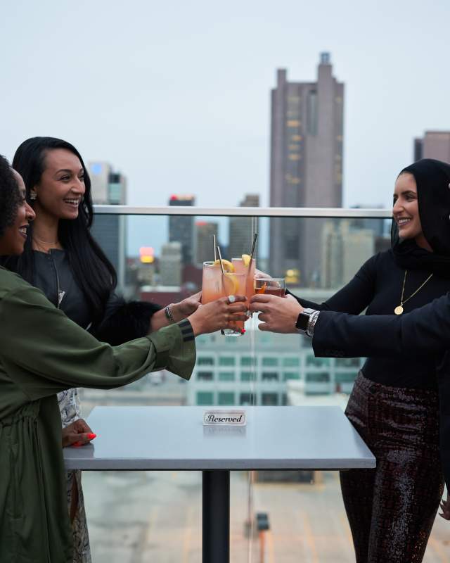 Four people clinking drinks on a rooftop bar in Columbus