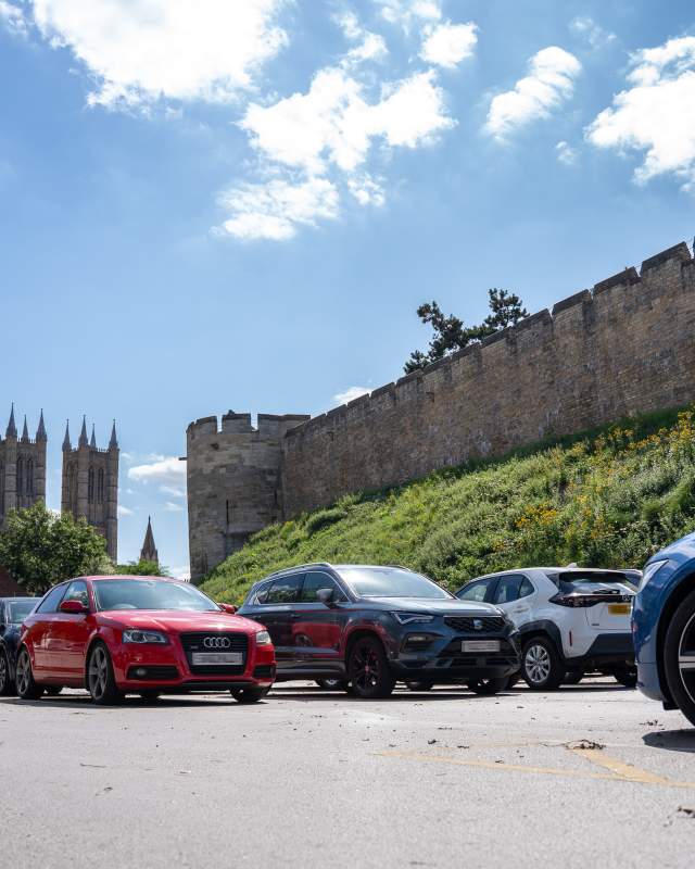 Castle Hill car park with cars in foreground and castle in background on sunny day
