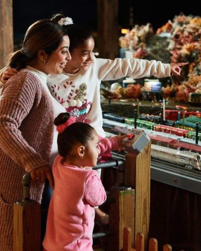 A woman with two small girls observing and pointing at a miniature train display decorated for the holidays at The Brandywine Museum of Art
