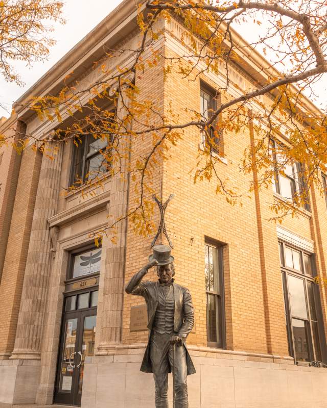 Historic brick building with autumn leaves in foreground. A statue of a President James Moore tipping his hat, creating a warm, nostalgic scene.