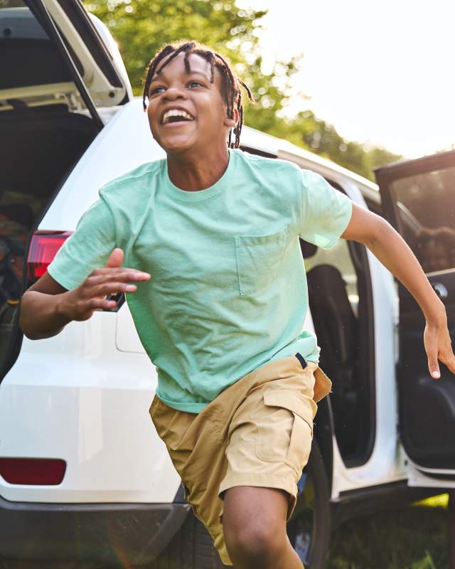 A young African-American boy exits a car with excitement.