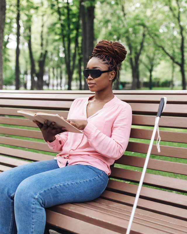 Blind woman sitting on park bench reading book in braille