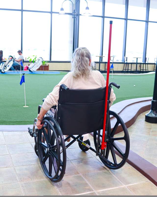 A woman in a wheelchair at the airport, positioned in front of an indoor putting green.