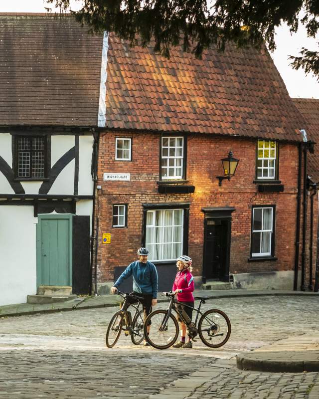 A couple of cyclists stood with bikes on the cobbled streets of Lincoln Steep Hill.