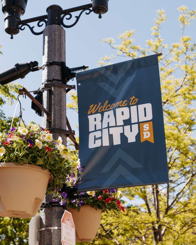Colorful flowers hanging on a flag pole with welcome sign in downtown rapid city, sd