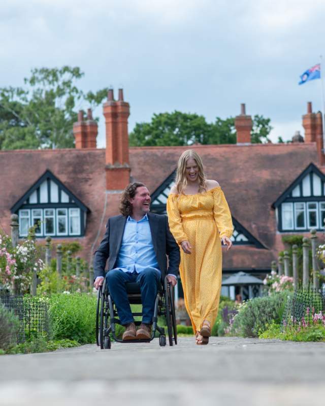 A man in a wheelchair and a woman laughing together on a path outside of Petwood Hotel