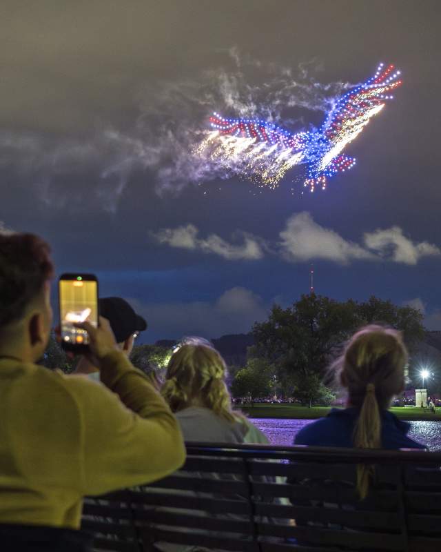 Spectators watch and photograph a red, white, and blue eagle-shaped drone show above Memorial Park in Rapid City.