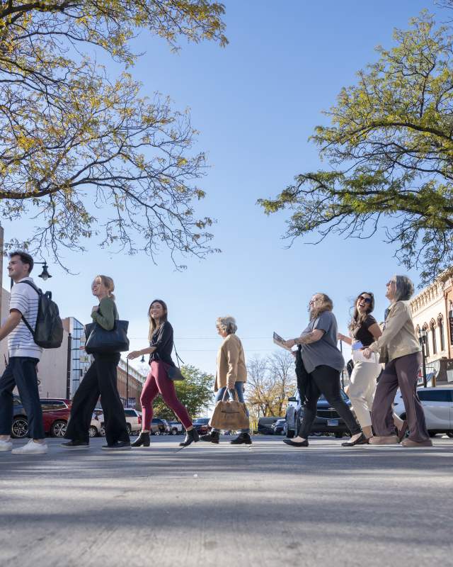 Conference attendees cross a tree-lined street in downtown Rapid City during a walking tour on a sunny fall day.