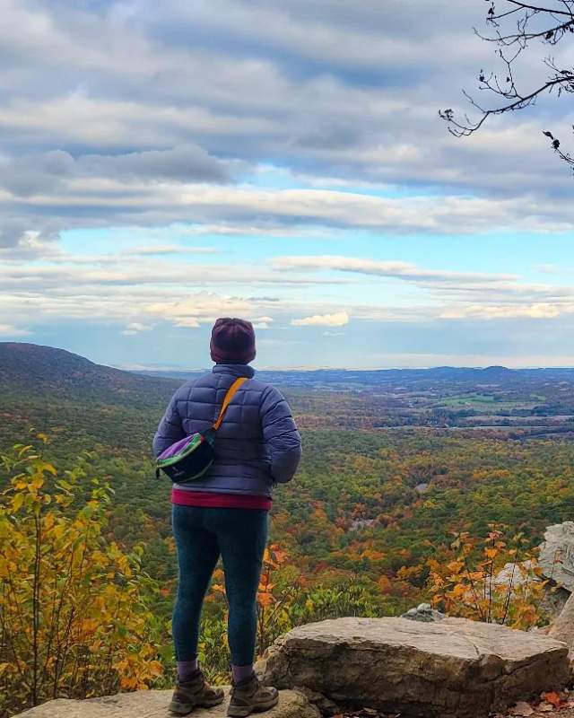 Person facing the scenery from the top of hawk mountain. The view is of trees beginning to change color