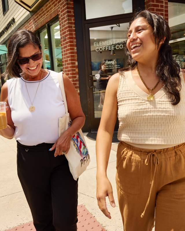 Two Hispanic women exit Elementary coffee shop in Harrisburg holding to-go cups and laughing
