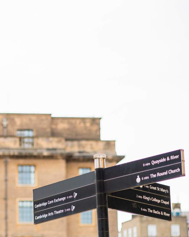A Cambridge signpost on the bottom right corner with an old yellow building blurred in the background