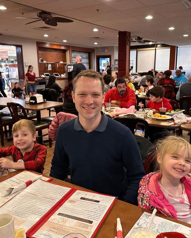 A family with two children smile while sitting at a table waiting for their meal