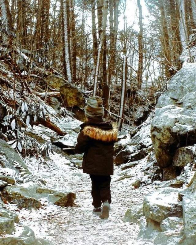 A young boy in a winter parka and hat walks with his back to the camera on a snow dusted trail at Hawk Mountain Sanctuary.