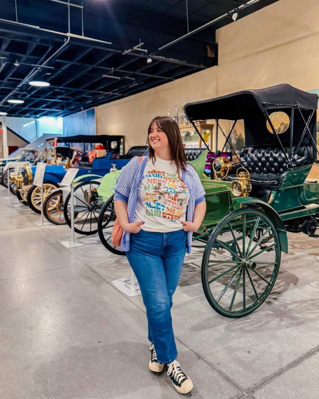 A woman poses in front of the antique cars at the Boyertown museum of historic vehicles